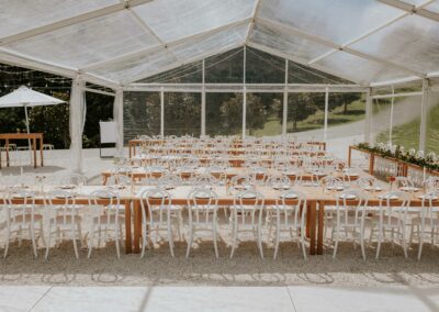 Clear marquee hire with transparent roof and sides set with white chairs, wooden tables with sun umbrellas and outdoor furniture hire. No people