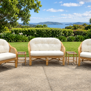 Outdoor wicker patio set with cream cushions on a concrete surface, a manicured lawn, and a blue sea and hills in the distance.